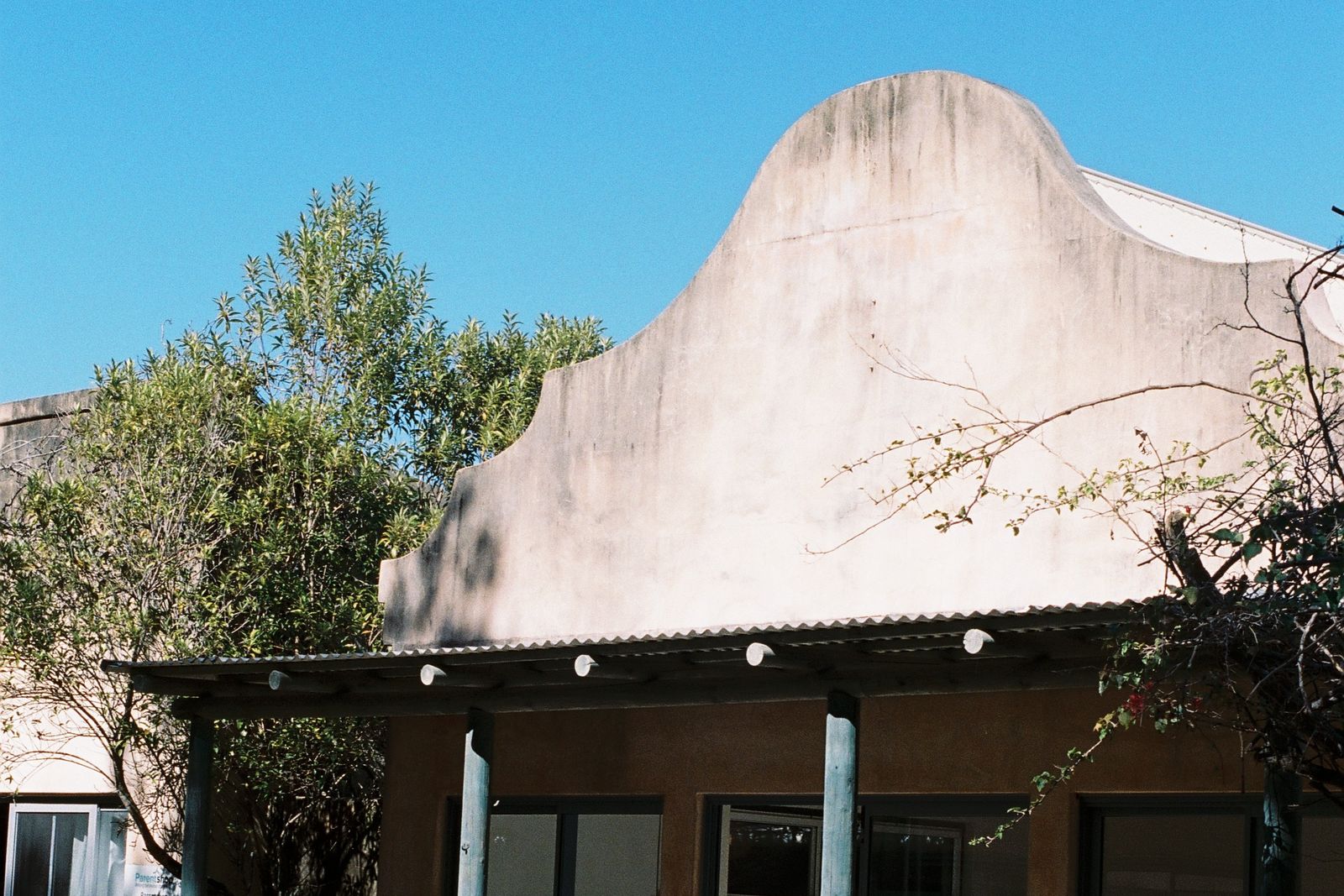 The front of Chalet Byron: a curved rendered parapet over a timber verandah, trees and blue sky