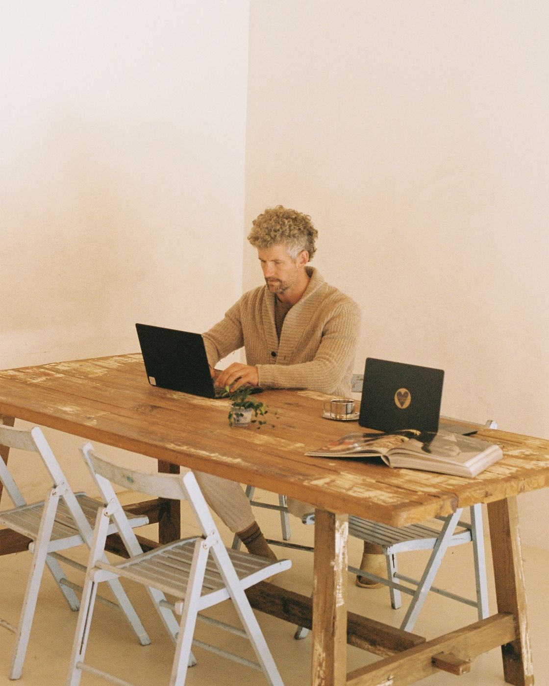 A member working on a laptop at the long trestle table, white folding chairs around it