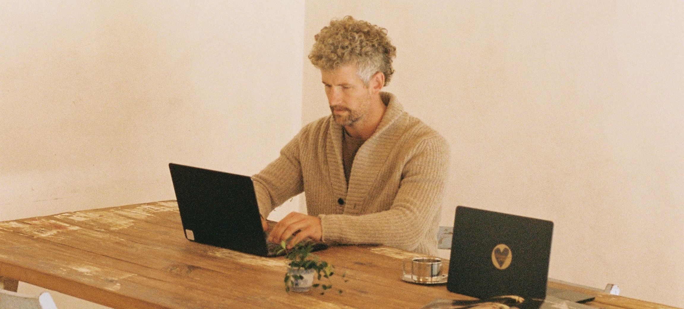 A member working on a laptop at the long trestle table, white folding chairs around it